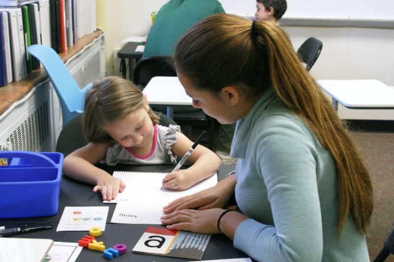 Student teacher helps child learning letters.